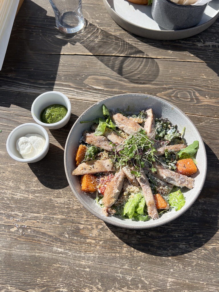 Grilled chicken salad served on a wooden table at Syn32 restaurant, with sunlight streaming across the plate