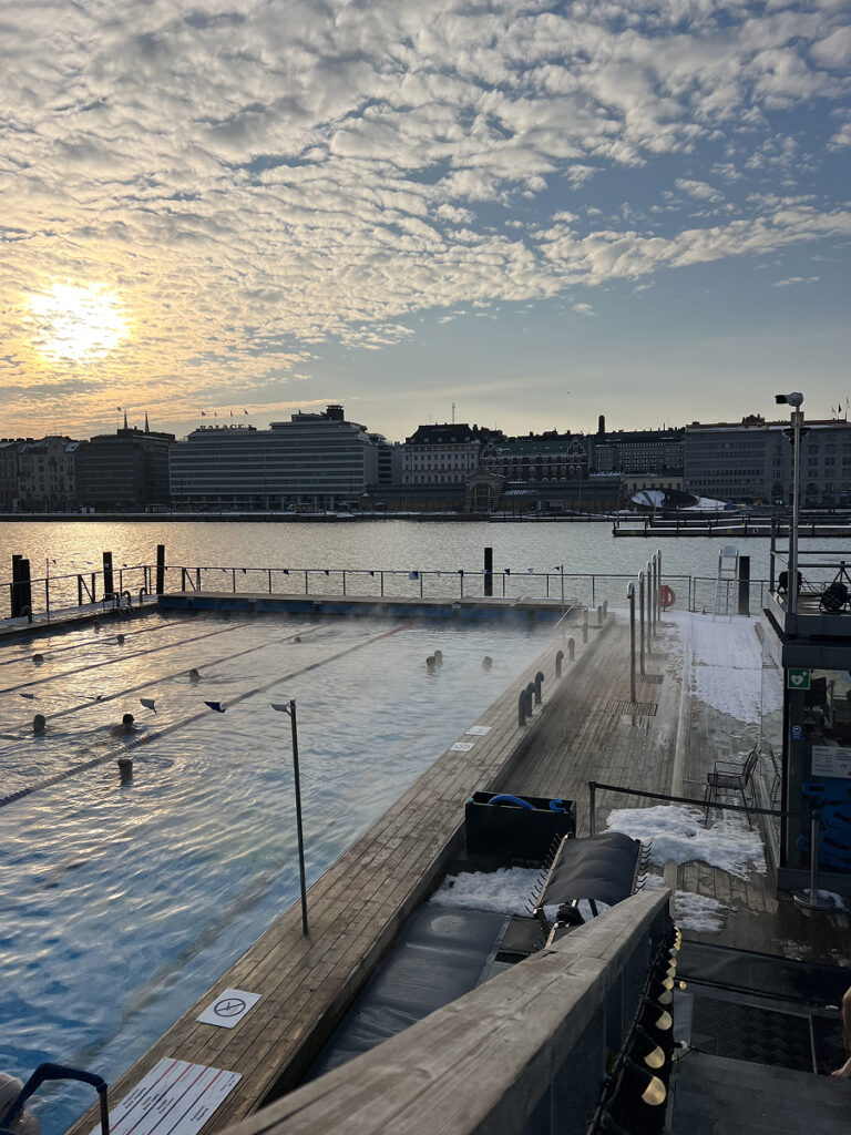Sunset over the heated outdoor pool at Allas Sea Pool in Helsinki during winter.