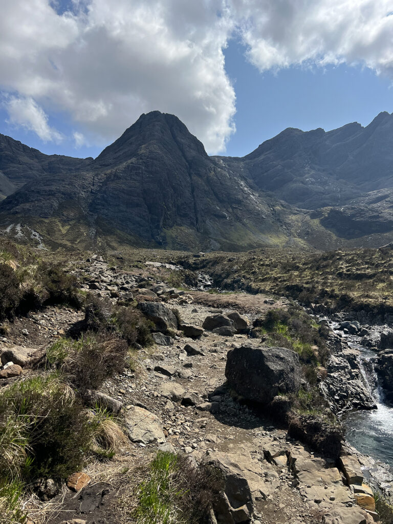 Rocky trail leading toward the dramatic Cuillin Mountains on the Fairy Pools hike, under a mix of sunshine and clouds on the Isle of Skye