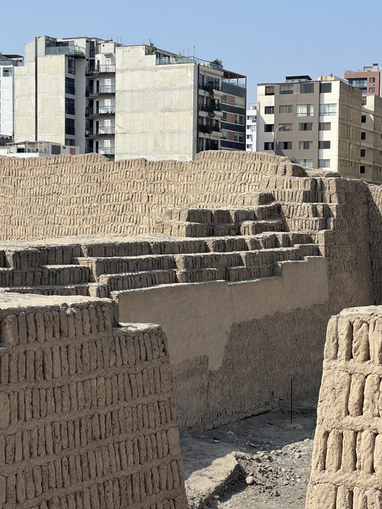 Pre-Incan adobe pyramid ruins of Huaca Pucllana in Lima, with modern apartment buildings in the background.