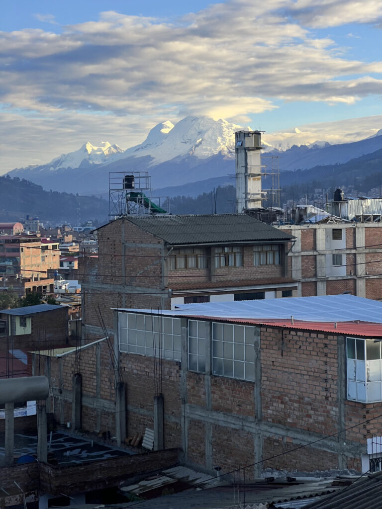 Morning view from an Airbnb rooftop in Huaraz, Peru, with rustic brick buildings in the foreground and the snow-capped Cordillera Blanca mountains glowing in the distance.