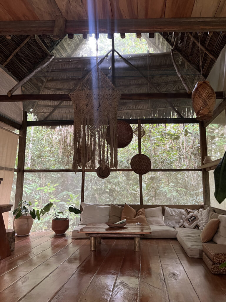 Rustic jungle Airbnb near Iquitos, Peru, with woven decor, wooden floors, and lush rainforest views through screened windows.