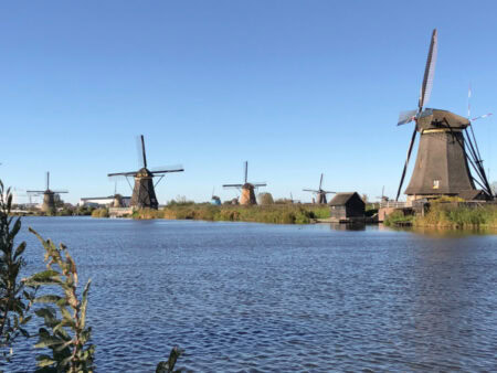 Historic windmills at Kinderdijk along the canal on a clear blue sky day — a top day trip from Amsterdam in the Netherlands