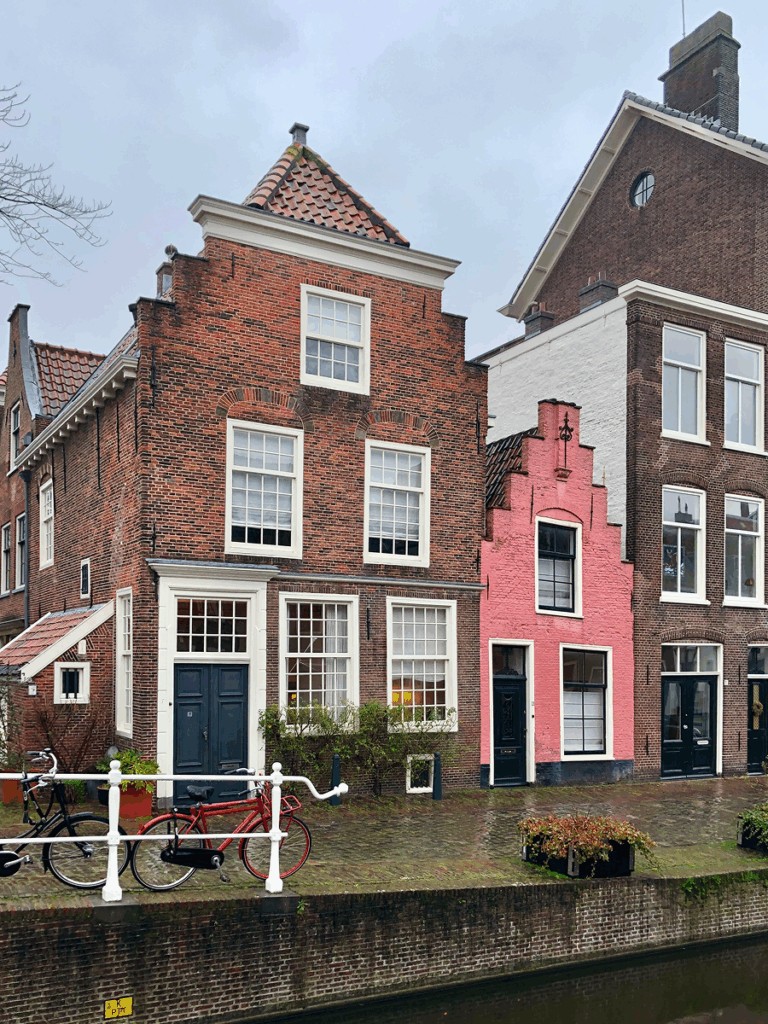 Colorful historic canal houses in Leiden, Netherlands, including a pink stepped-gable facade on a quiet cobbled street