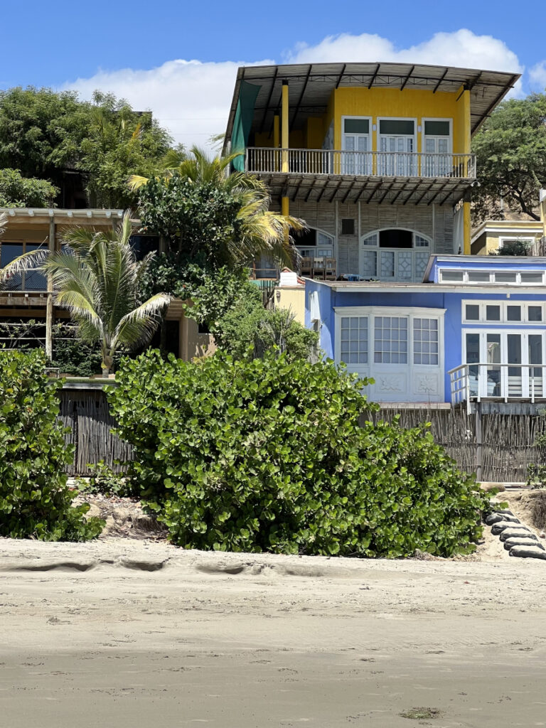 Colorful beachfront houses in Mancora, Peru, framed by lush greenery and sandy shore.