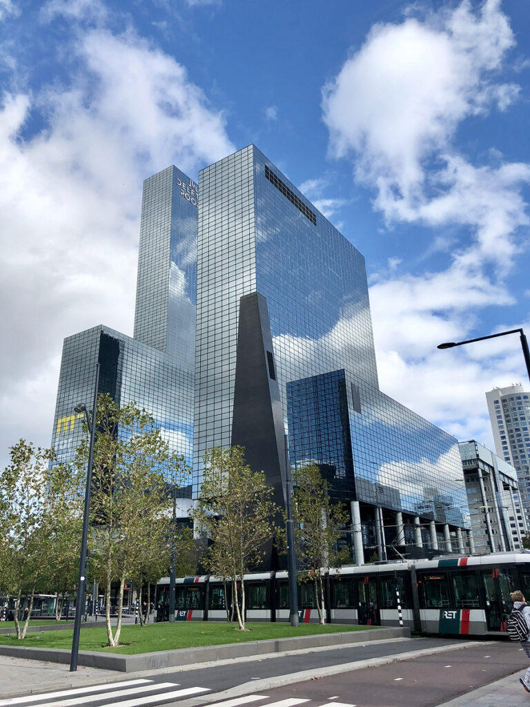 Modern glass skyscraper and tram in Rotterdam, Netherlands, showcasing contemporary Dutch architecture