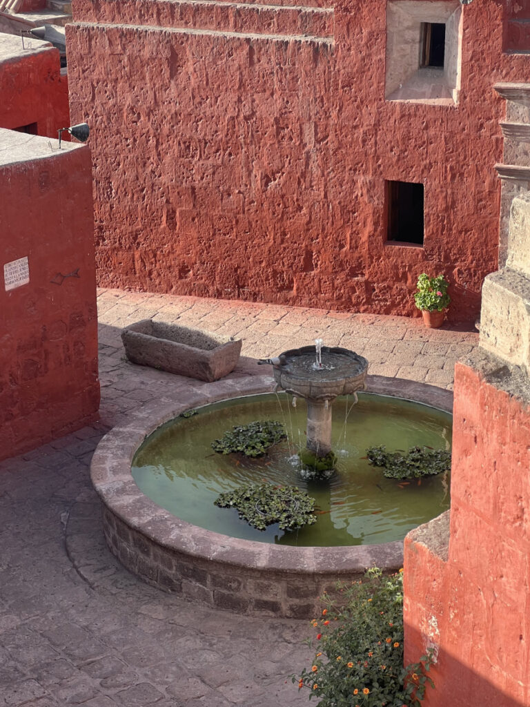 Vibrant red courtyard with a circular fountain and stone bench inside the Santa Catalina Monastery in Arequipa, Peru.