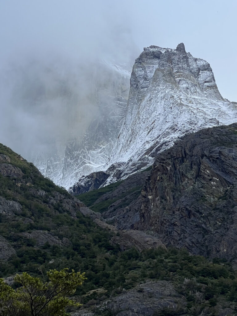 Dramatic view of a snow-covered granite spire shrouded in clouds, seen from the O Circuit trail in Torres del Paine National Park
