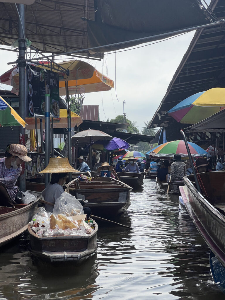 Boats selling food and souvenirs at a colorful floating market in Thailand, with vendors in traditional hats