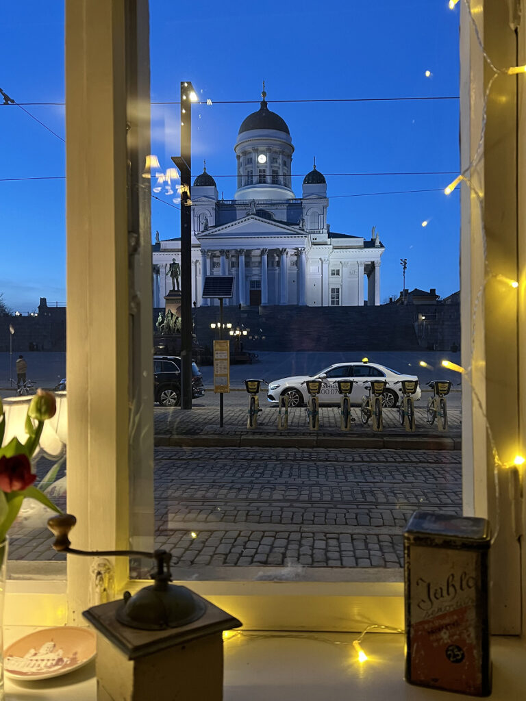 Helsinki Travel Guide – night view of Helsinki Cathedral from a window table at Ravintola Savotta, with fairy lights and vintage decor in the foreground.