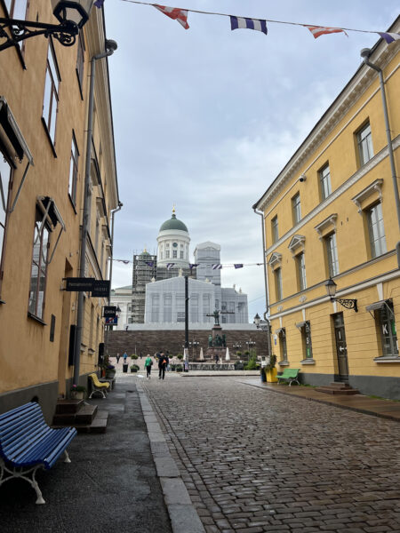 Cobblestone street in Helsinki leading to Senate Square with Helsinki Cathedral in the background on a cloudy day.