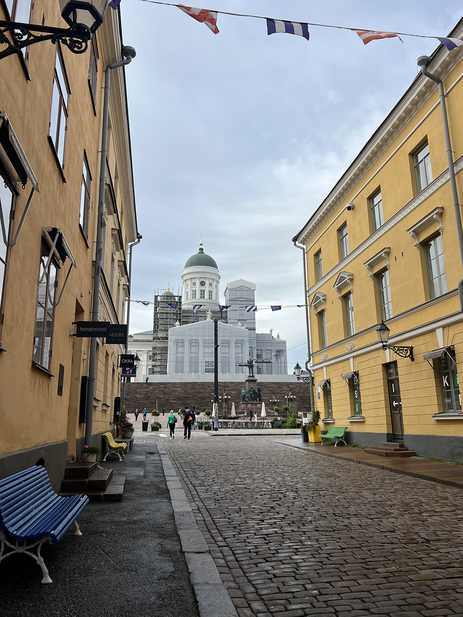 Cobblestone street in Helsinki leading to Senate Square with Helsinki Cathedral in the background on a cloudy day.
