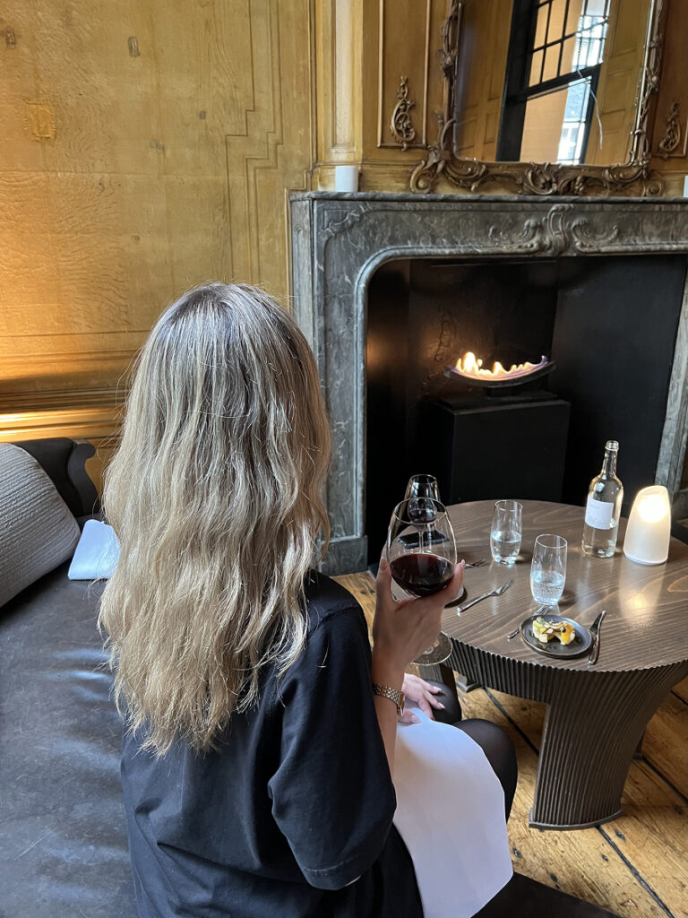 Guest enjoying High Wine at The Dylan Amsterdam seated by the fireplace with a glass of red wine