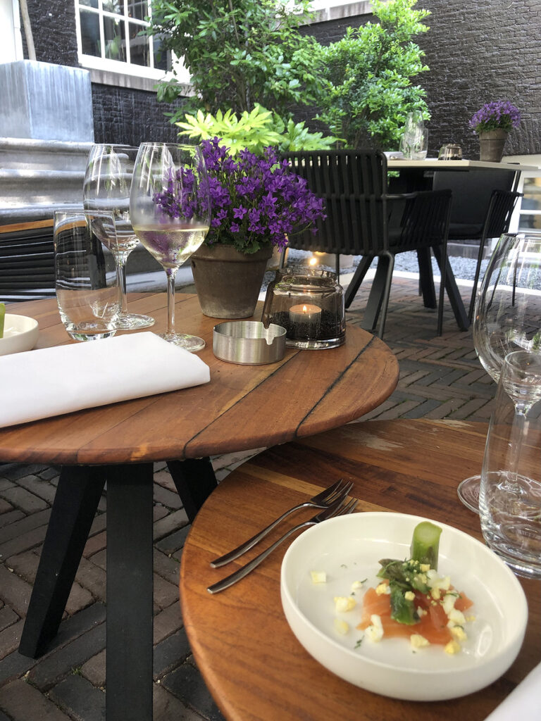 Courtyard table at The Dylan Amsterdam set with wine glasses, flowers, and a smoked salmon starter during High Wine