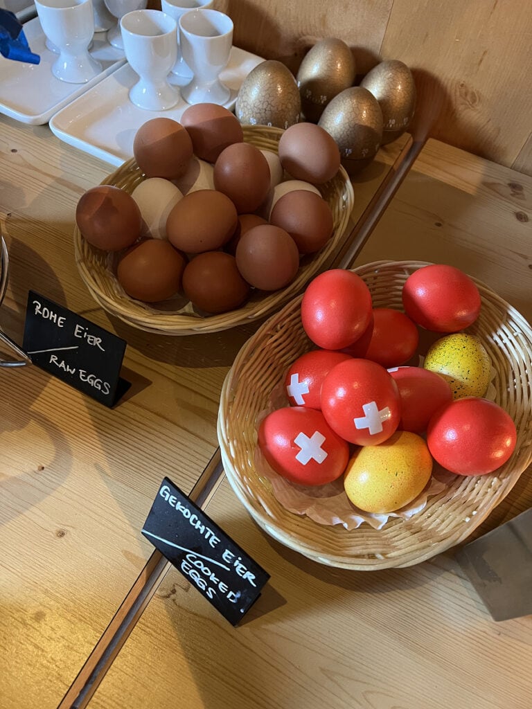 Breakfast buffet at Hotel Capricorn Zermatt with baskets of eggs, including red boiled eggs painted with the Swiss cross.