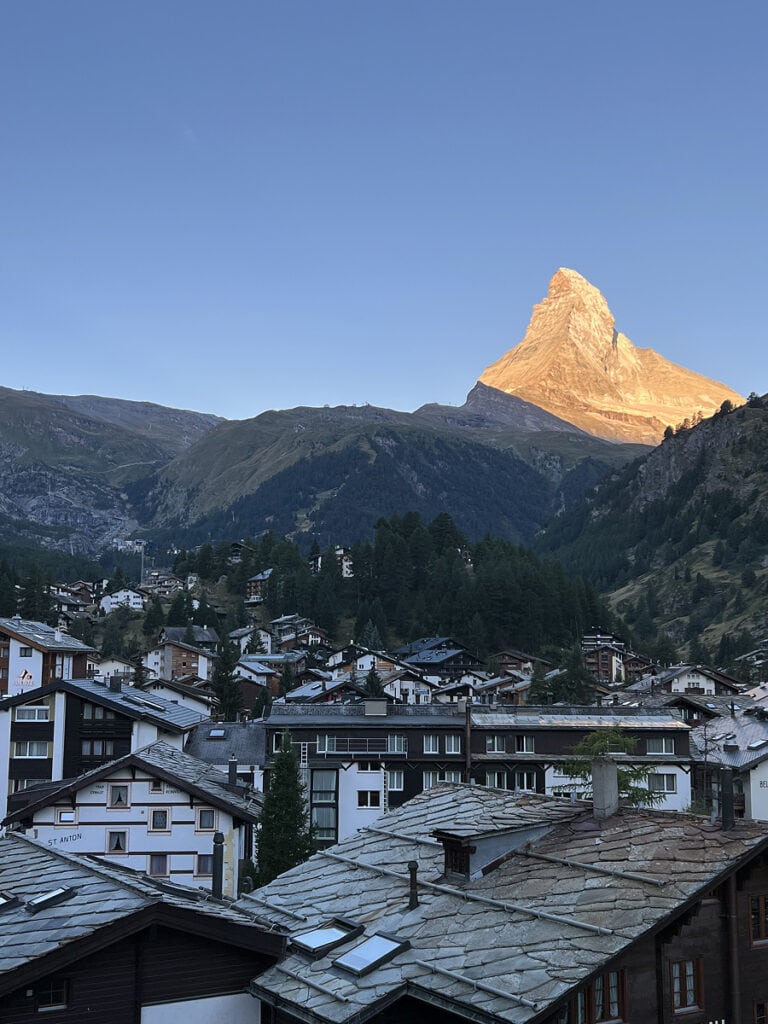 Sunrise over the Matterhorn seen from Hotel Capricorn Zermatt balcony, with alpine village rooftops in the foreground.