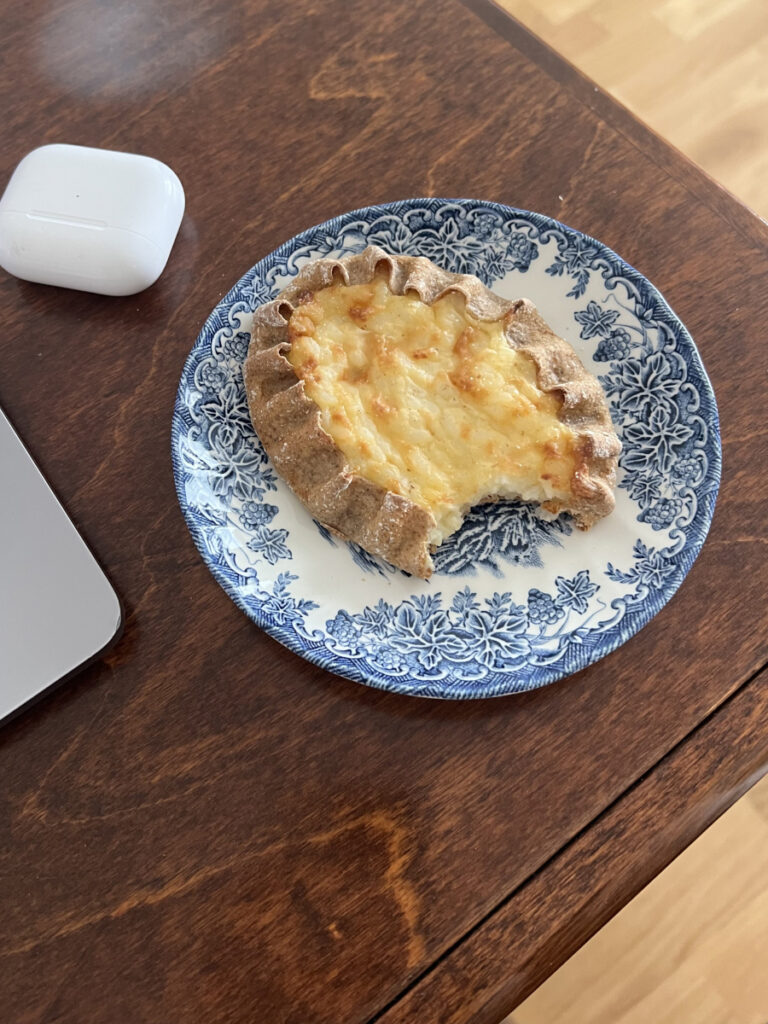 Traditional Finnish Karelian pie with rice filling on a blue and white plate, partially eaten, served as a snack.