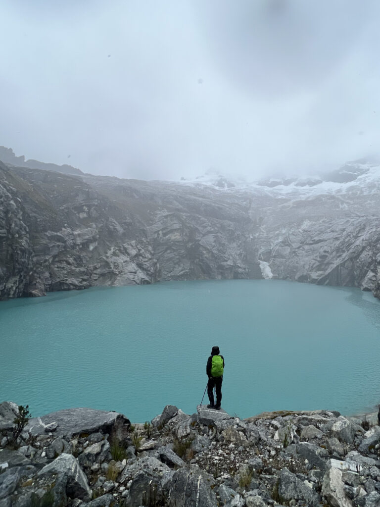 Hiker overlooking the turquoise waters of Laguna 513 in Huascarán National Park on a cloudy day