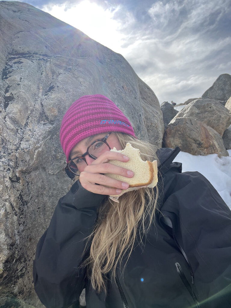 Woman eating a sandwich behind a rock to shelter from strong wind during the Laguna de los Tres hike in El Chaltén, Patagonia