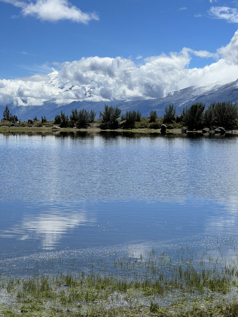 Laguna Radian hike near Huaraz, Peru, with reflective lake and distant mountains under blue skies.