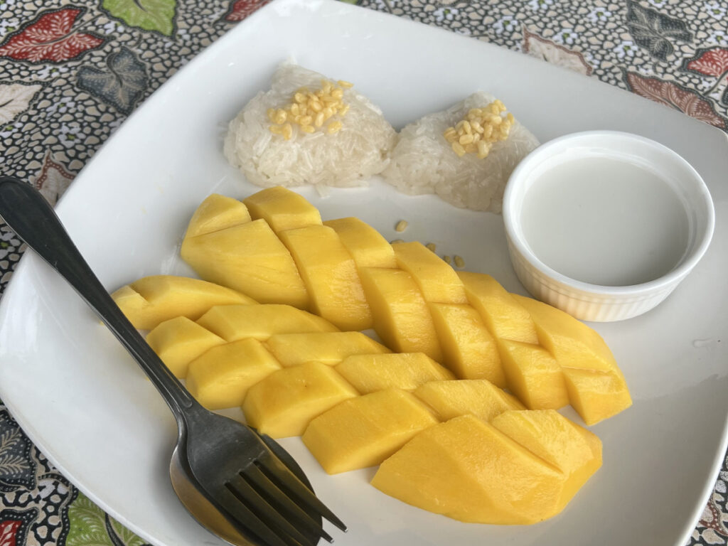 A plate of traditional Thai mango sticky rice served with sweet coconut sauce on a patterned tablecloth