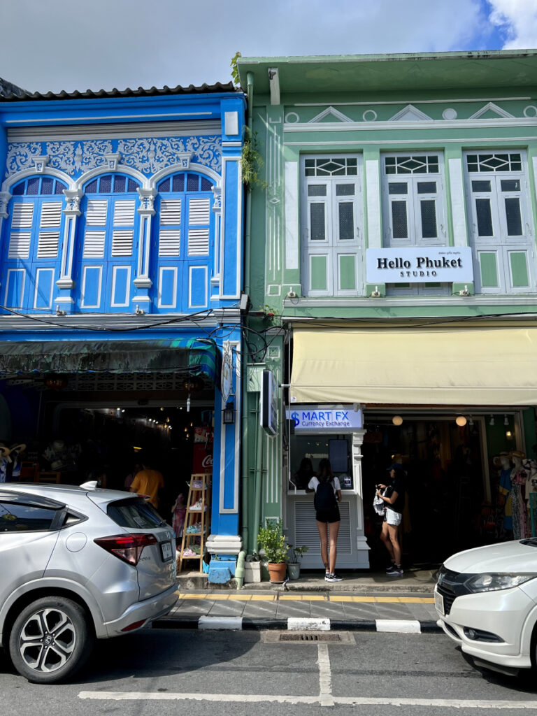 Colorful colonial-style shophouses in Phuket Old Town, Thailand, with blue and green facades and a small boutique storefront.