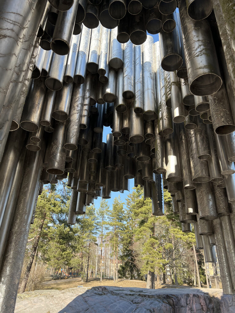 Close-up view of the Sibelius Monument’s steel pipes in Helsinki, Finland, with a backdrop of pine trees and blue sky.