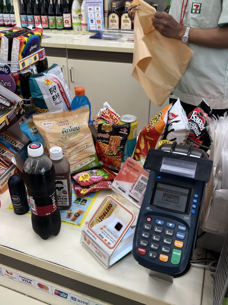 A counter full of snacks, drinks, and convenience items at a 7-Eleven in Thailand, showing the wide variety of local treats