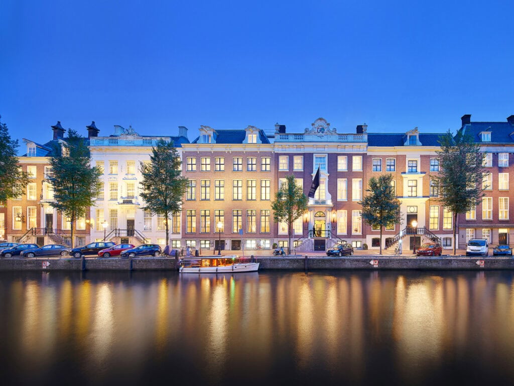 Waldorf Astoria Amsterdam exterior — six canal palaces on Herengracht illuminated at dusk