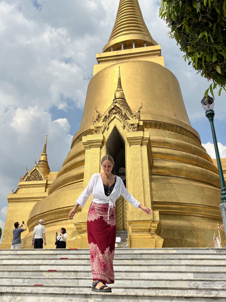 Woman wearing modest attire in front of the golden stupa at Wat Phra Kaew, Bangkok's Grand Palace